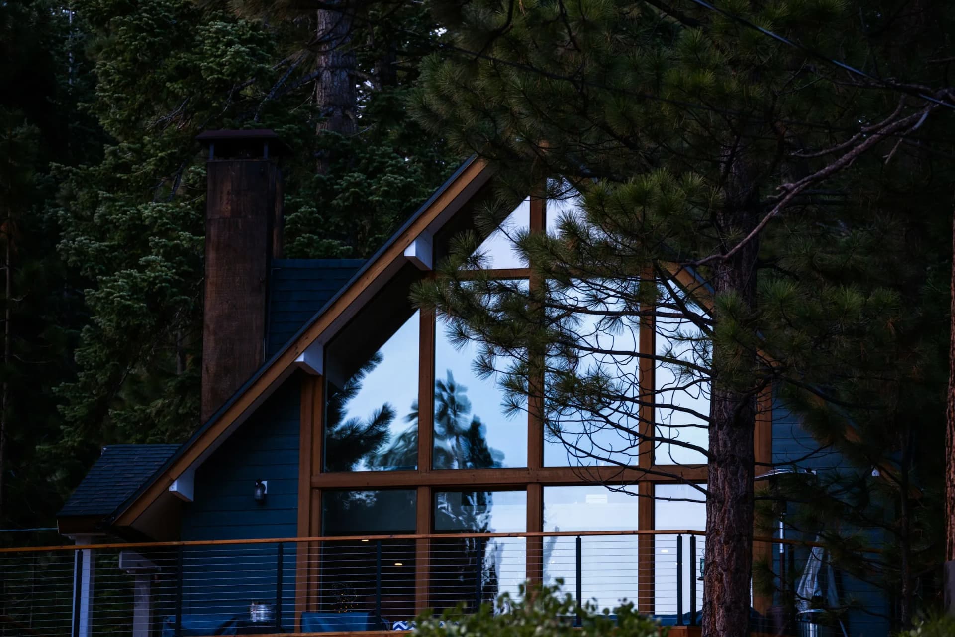 Modern timber A-frame home glowing at dusk in a pine forest