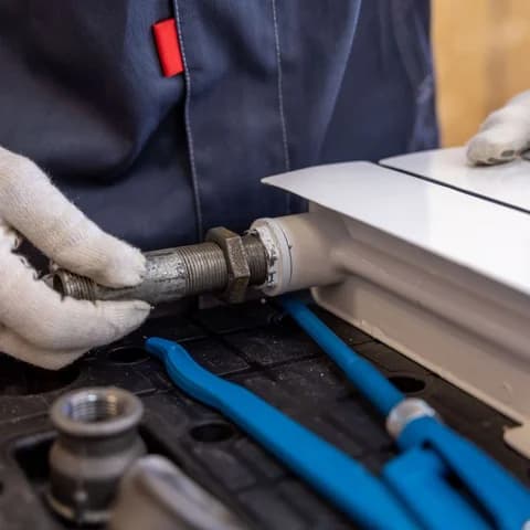 Gloved hands fitting a radiator pipe with hand tools