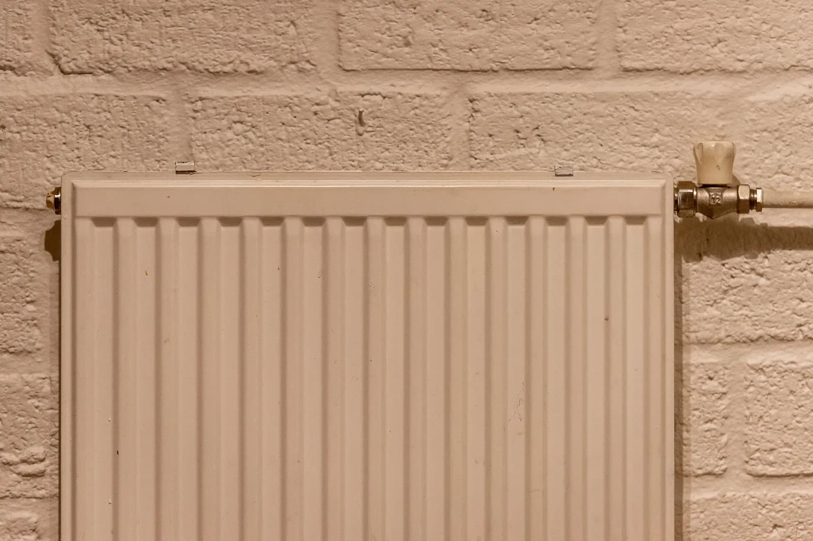 White panel radiator mounted on an exposed brick wall, with a chrome shutoff valve.