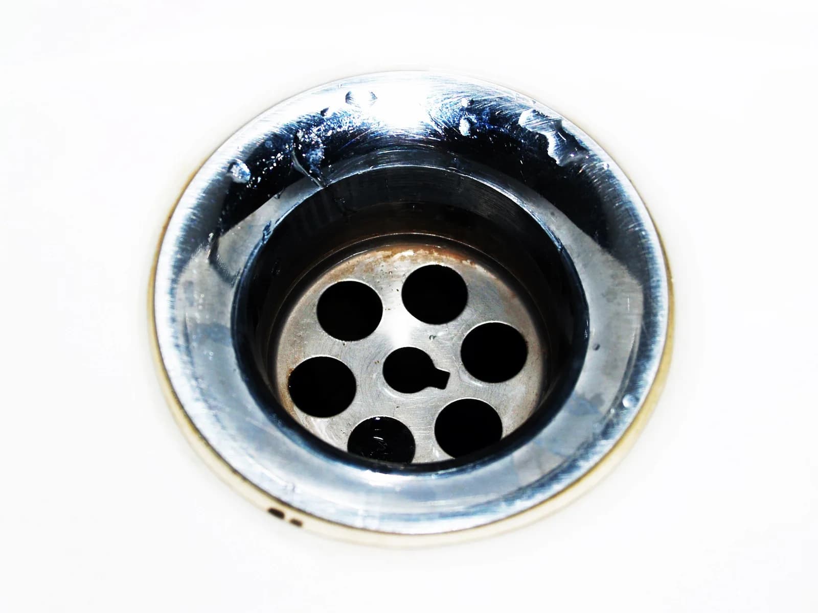 Close-up of a chrome kitchen sink drain and strainer basket with water droplets.