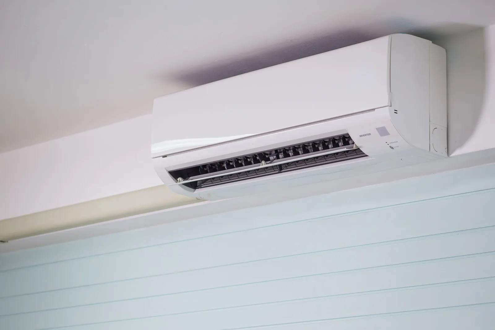 Close-up of a white ductless mini-split indoor head unit mounted high on a ceiling-height wall inside a home.