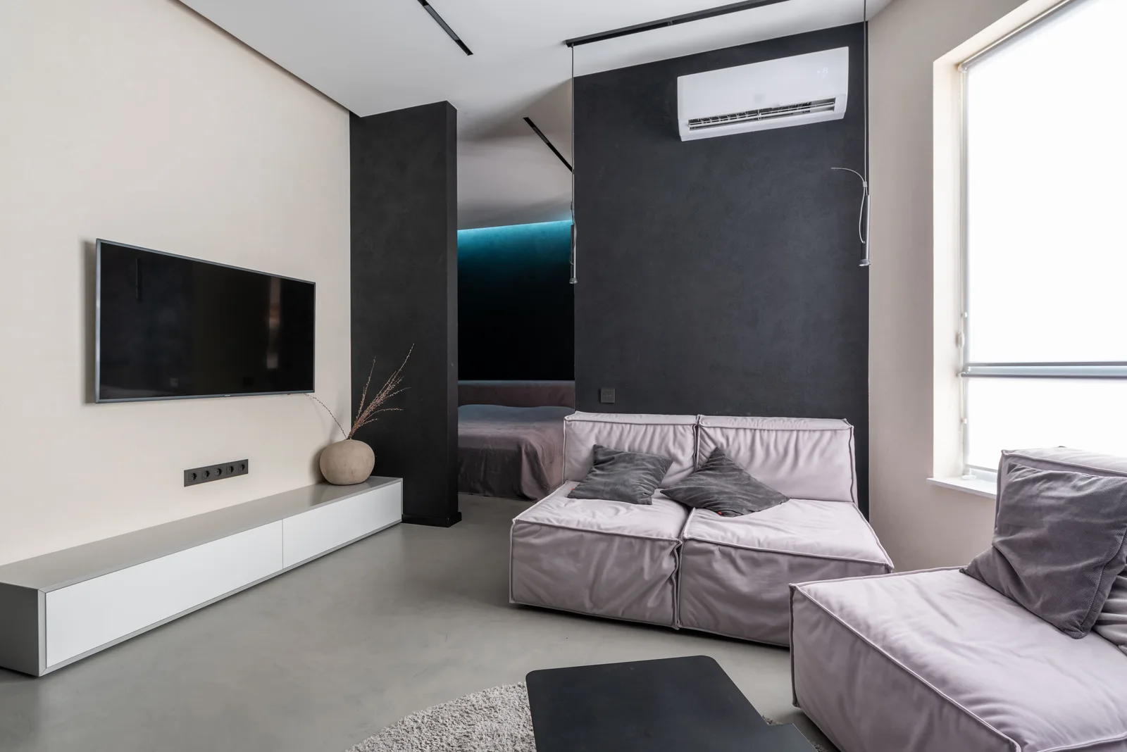 A ductless mini-split indoor unit mounted on a dark accent wall above a sofa in a modern living room.